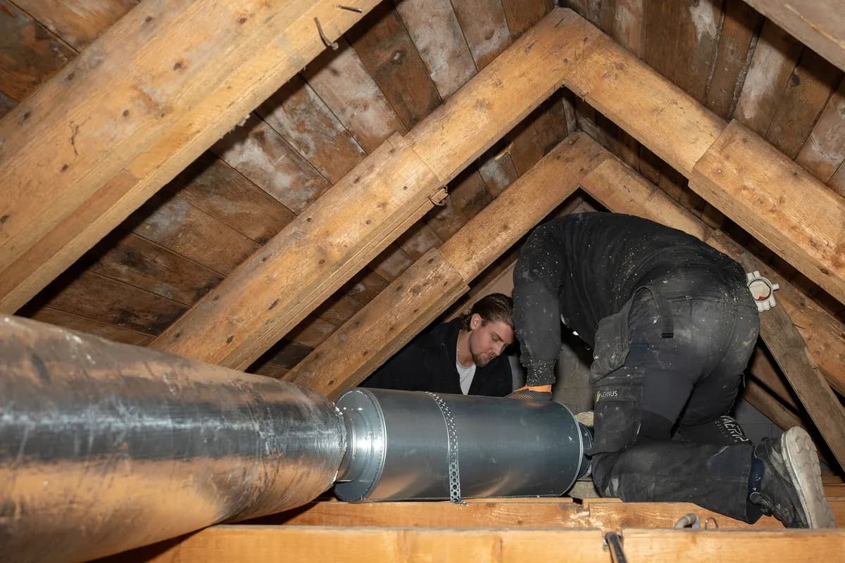 Två ventilationstekniker som monterar en stor kanal på en vind vid FTX-installation i Stockholm